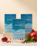 Pack de 3 cajas de Ayllu sobre una mesa de mármol, junto a una fruta de granada.